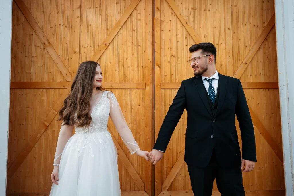 Mihaela & Mihai — Cuplul ținându-se de mână în fața ușilor de lemn.